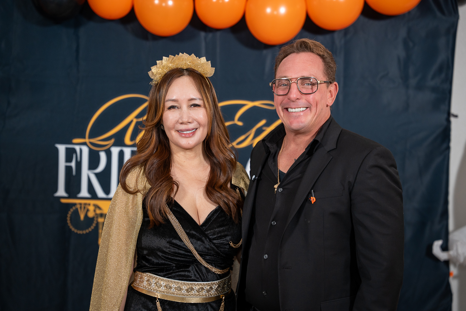 Two friends smiling at the REFC backdrop beneath the Halloween balloons