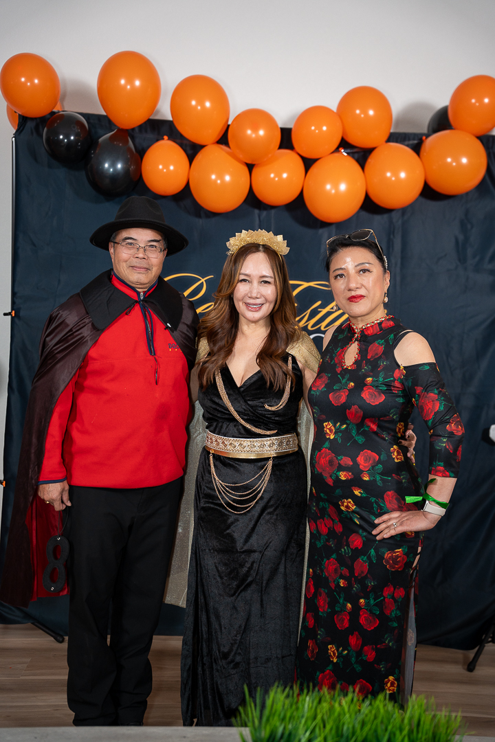 Three costumed guests posing beneath the orange and black balloons