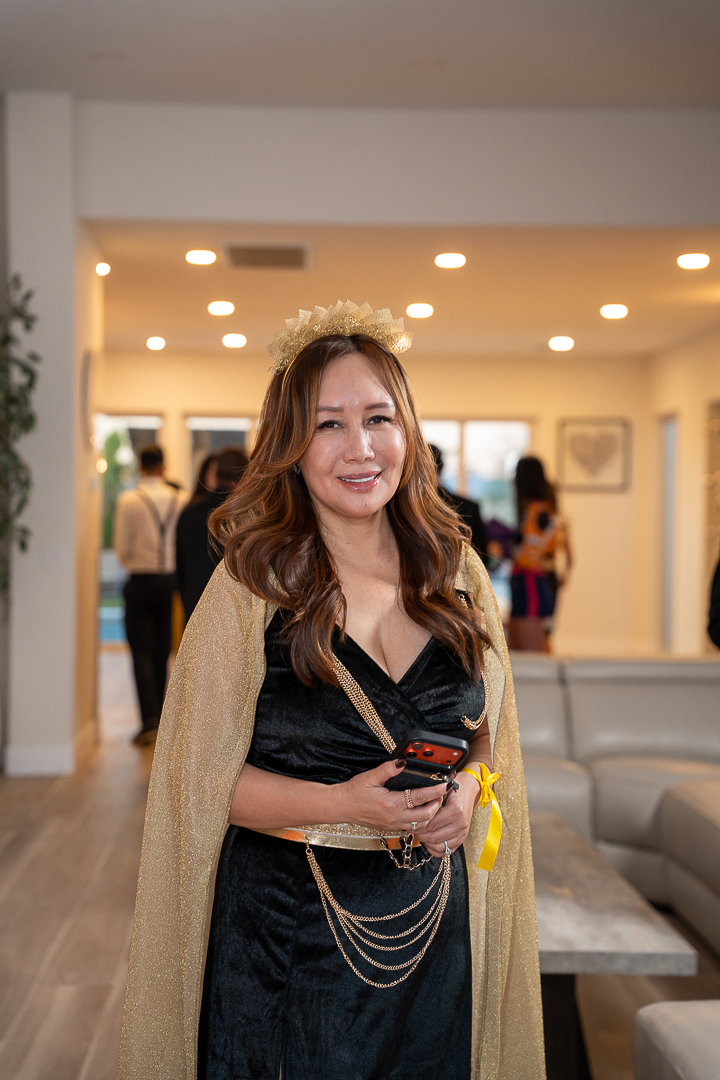 A guest in a black-and-gold gown smiling as she arrives at the celebration