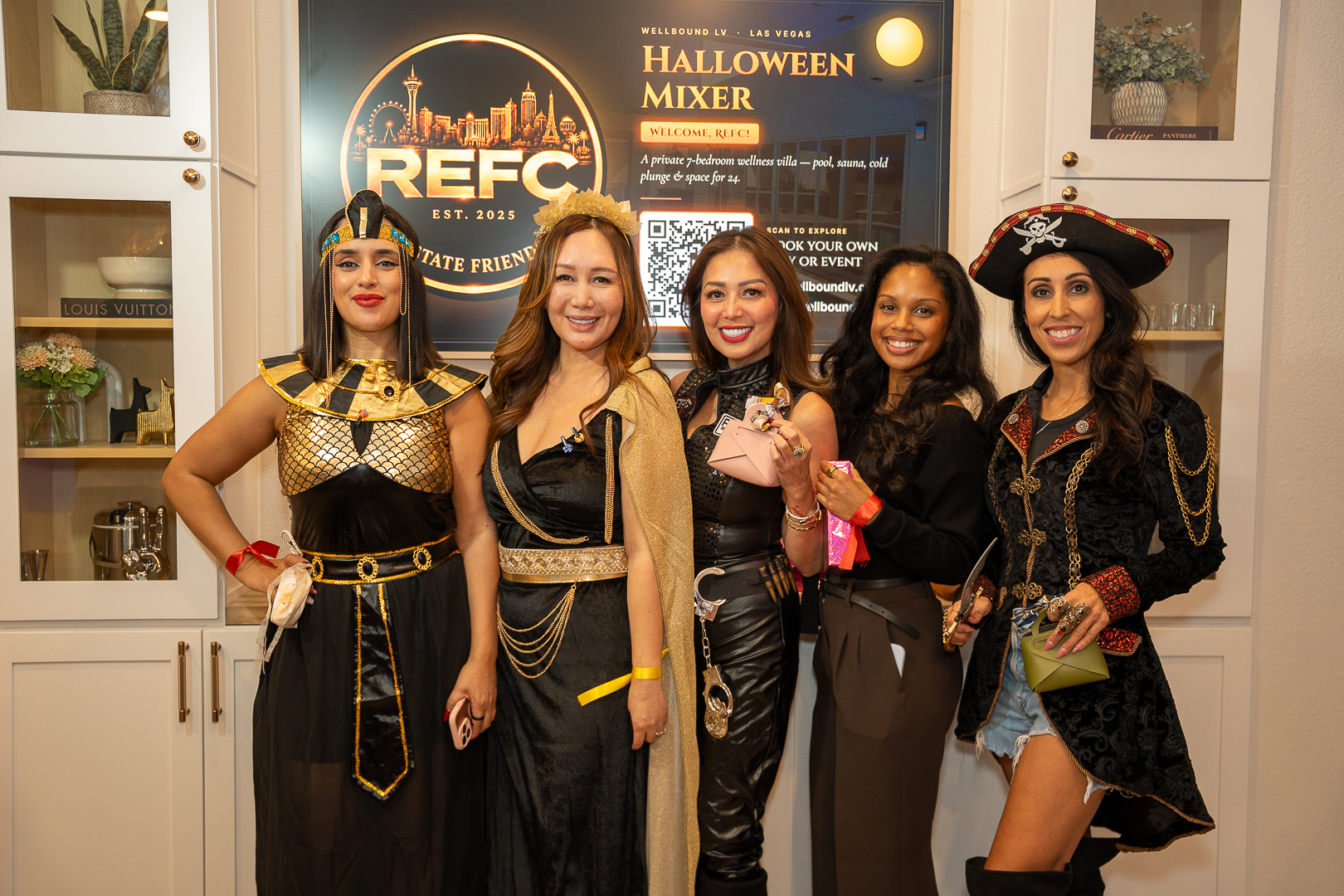 Five friends in Halloween costumes posing beside the REFC mixer sign