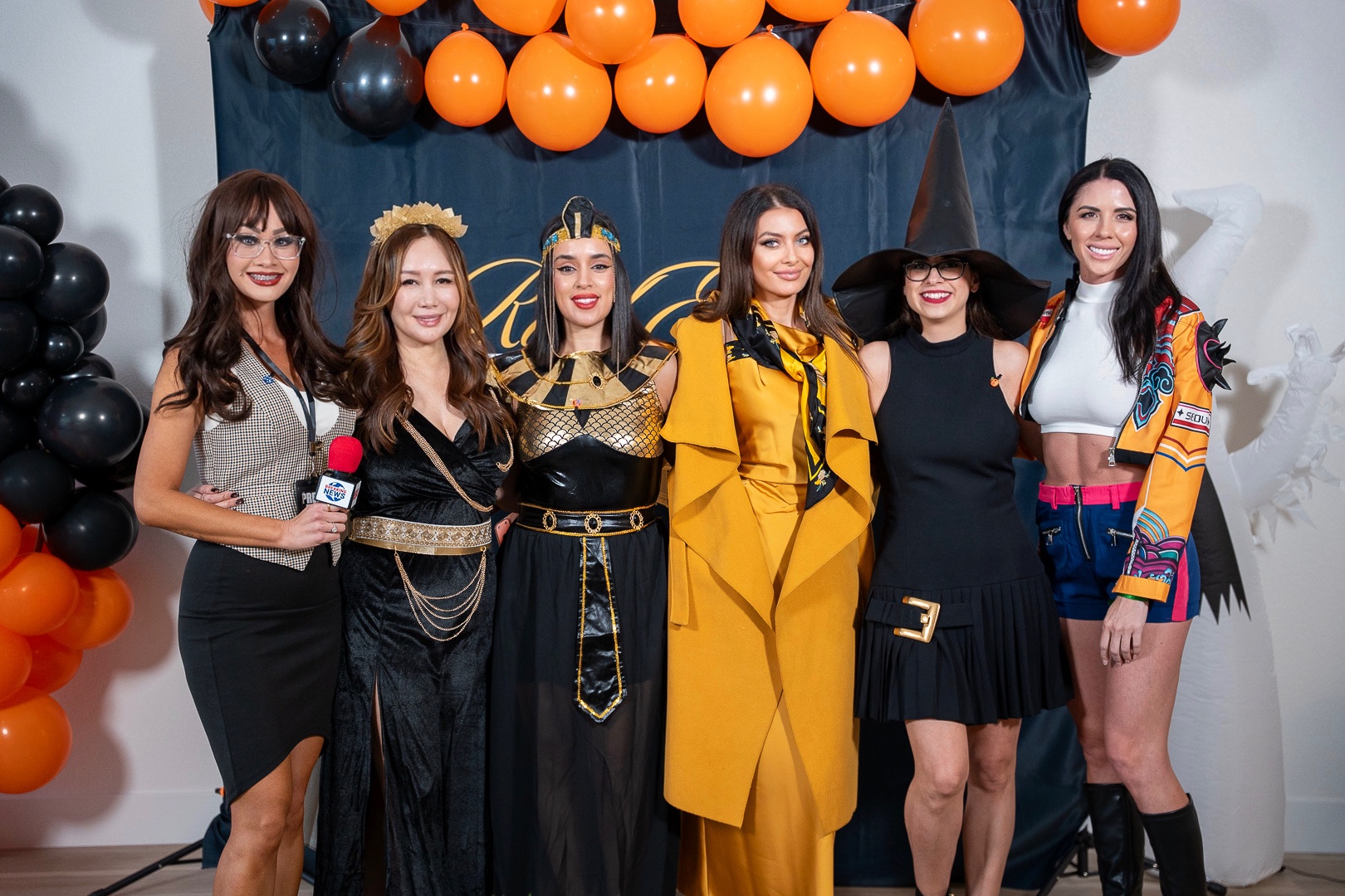 Six costumed friends smiling together at the REFC anniversary backdrop, an inflatable ghost rising behind them
