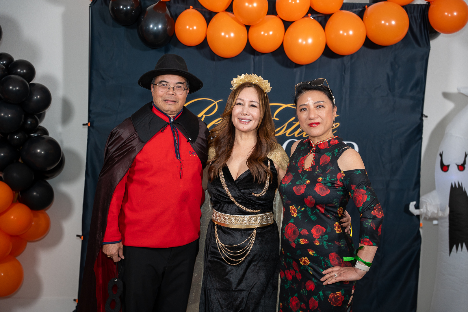 Three costumed friends smiling together at the REFC balloon backdrop