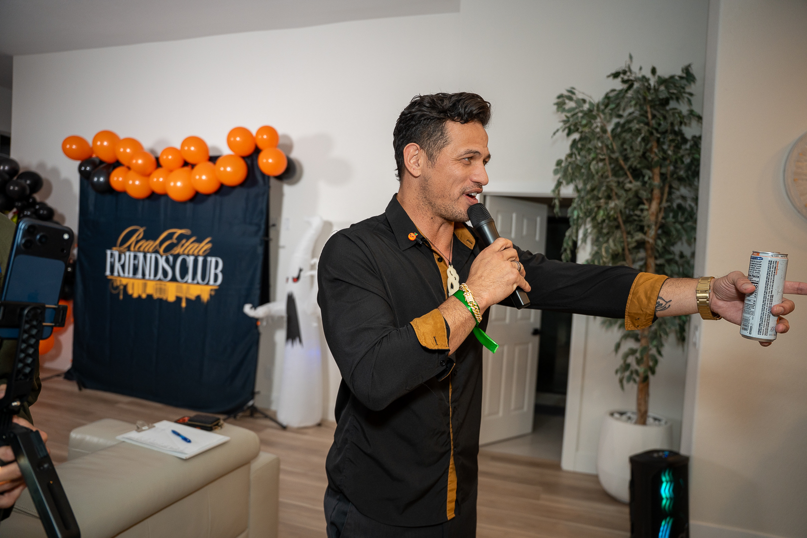 A suited guest holding the microphone and a drink beside the backdrop
