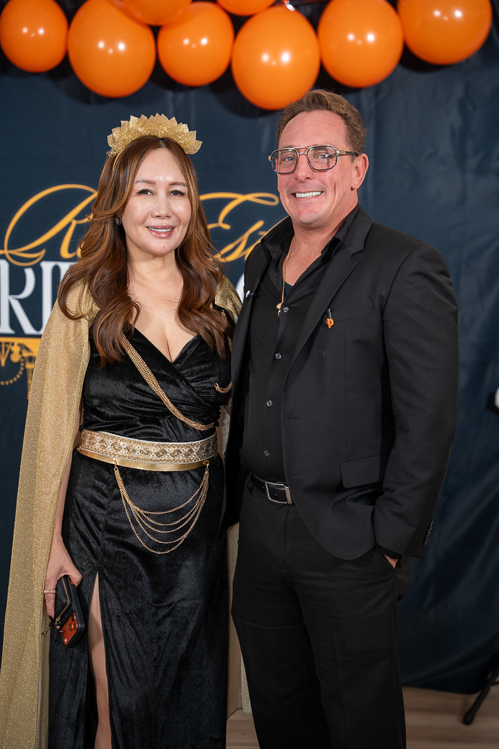 Two guests in black outfits posing at the REFC anniversary backdrop