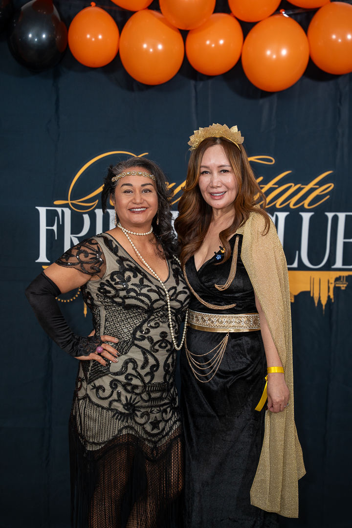 A close portrait of two smiling friends at the REFC anniversary backdrop