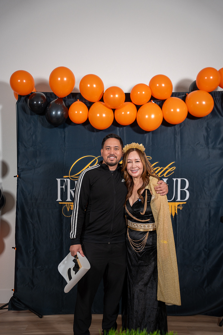 Two costumed friends posing together at the Real Estate Friends Club backdrop