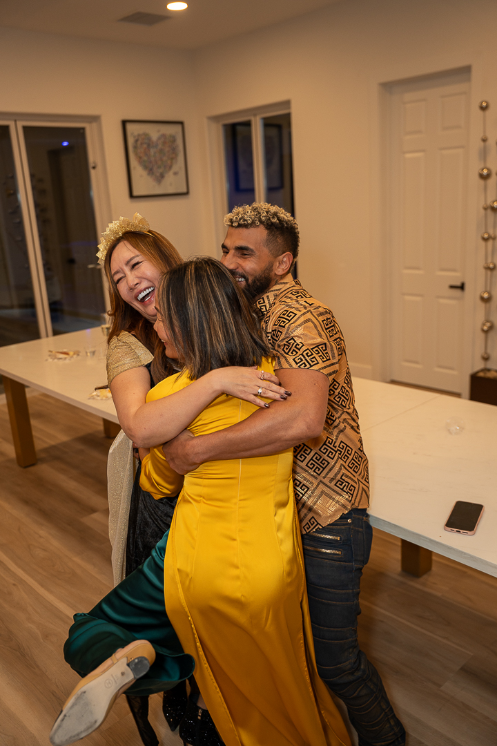 Three friends laughing and embracing during the anniversary party