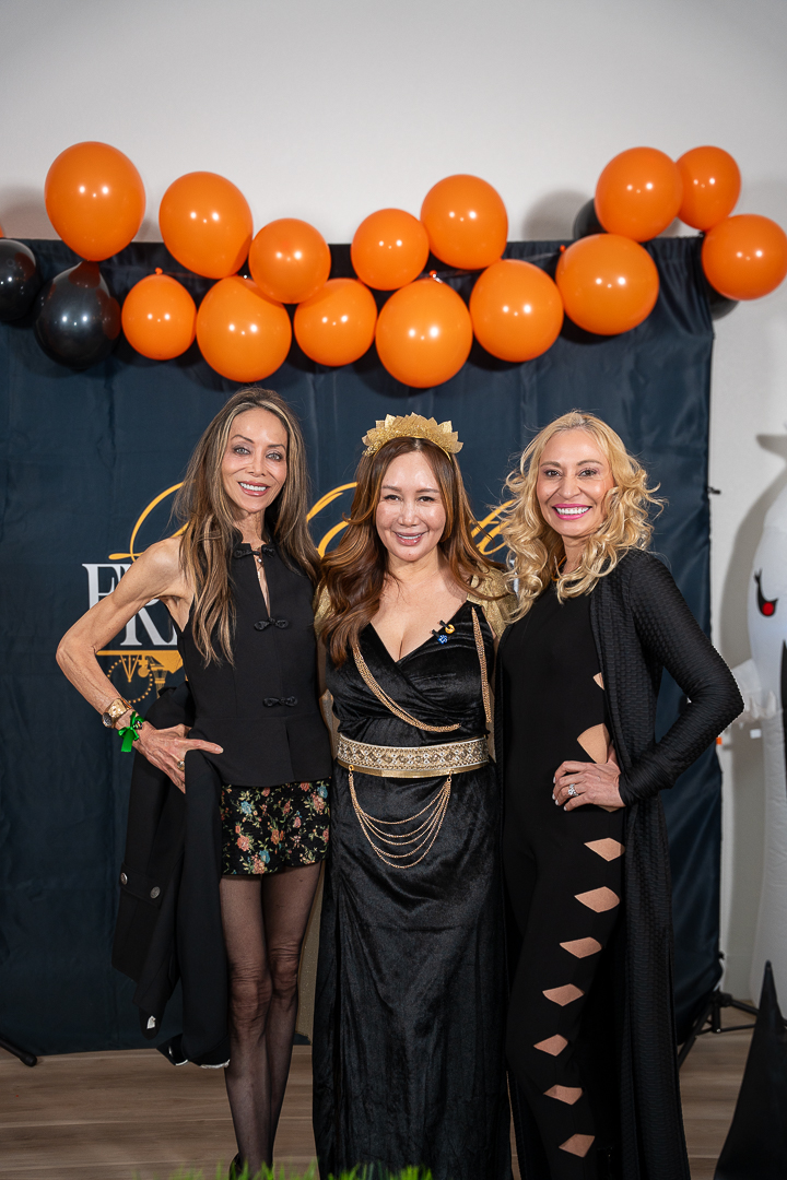 Three smiling guests in black and gold outfits posing at the REFC anniversary backdrop