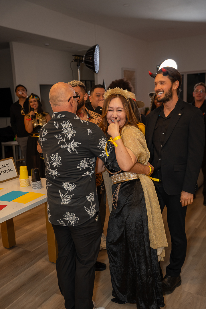 A smiling guest in a gold crown embracing a friend beside the kitchen island
