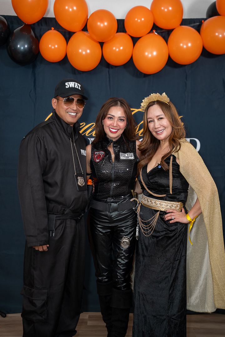 Three costumed friends posing beneath the orange and black balloons