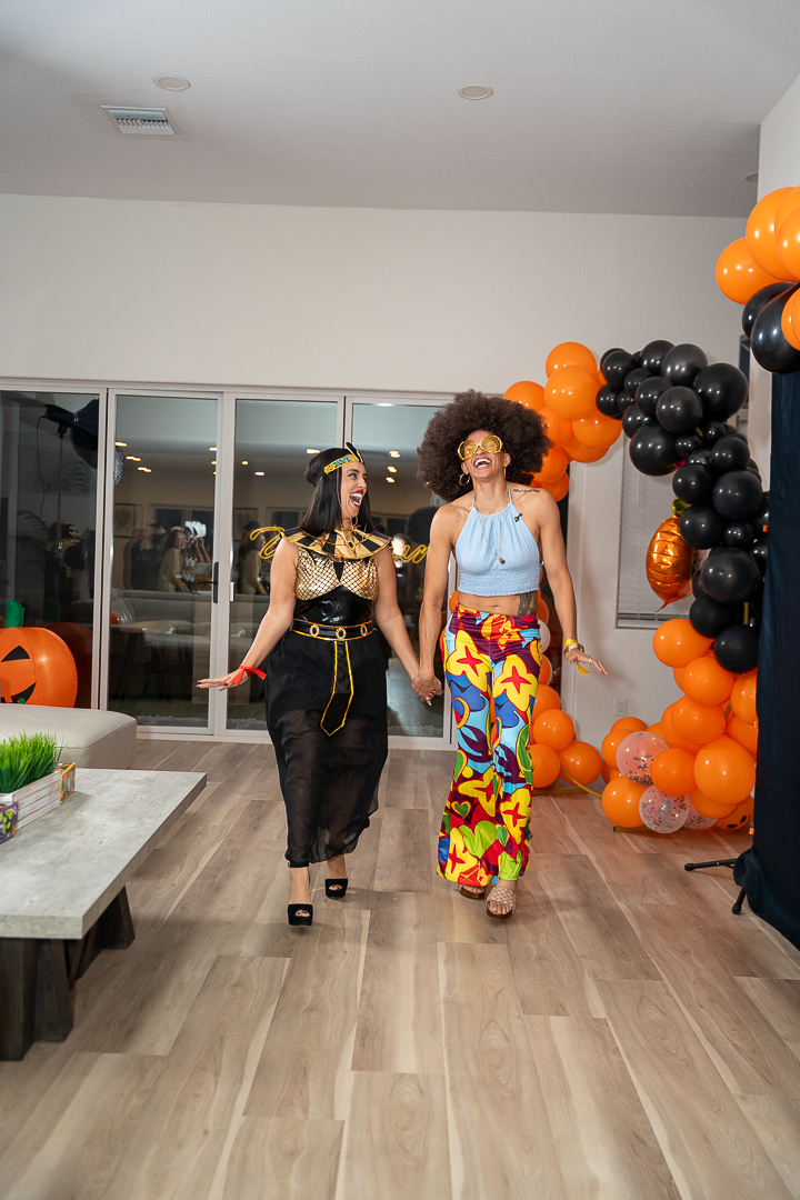 Three costumed friends walking past the pumpkin and balloon arch