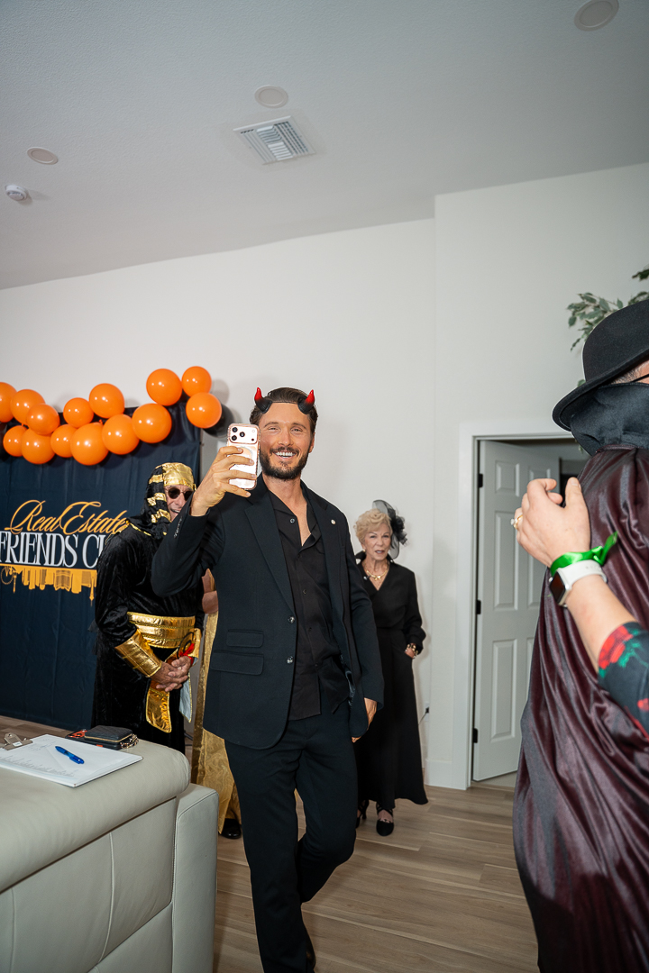 A guest in a dark suit raising a drink beneath the Halloween balloons