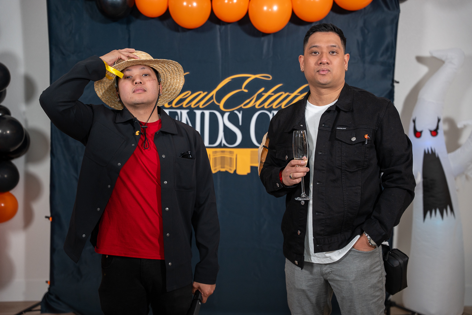 Two guests in matching jackets and a straw hat posing at the REFC backdrop with a microphone