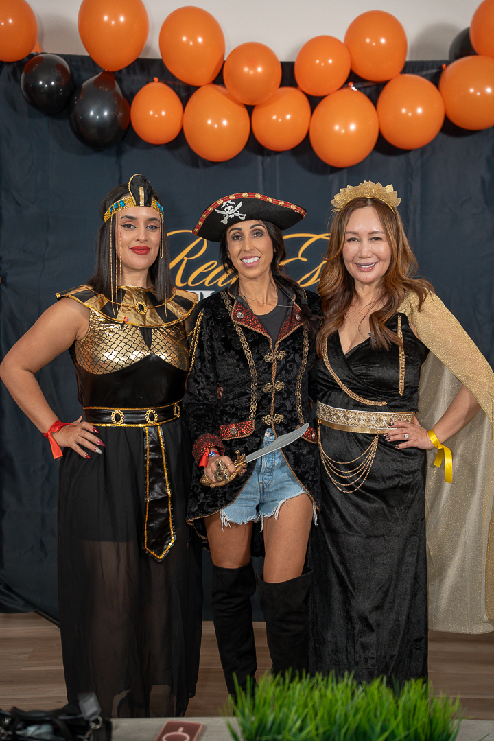 Three friends in Egyptian-inspired and pirate costumes posing beneath Halloween balloons