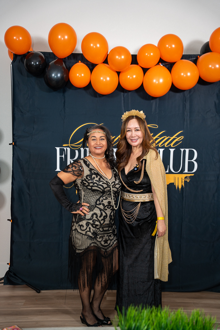 Two friends posing in patterned and black-and-gold outfits beneath the REFC balloons