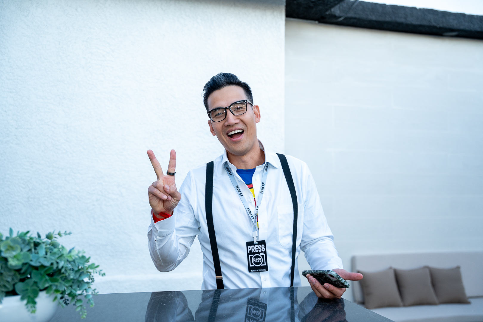A guest in suspenders and a press badge flashing a peace sign