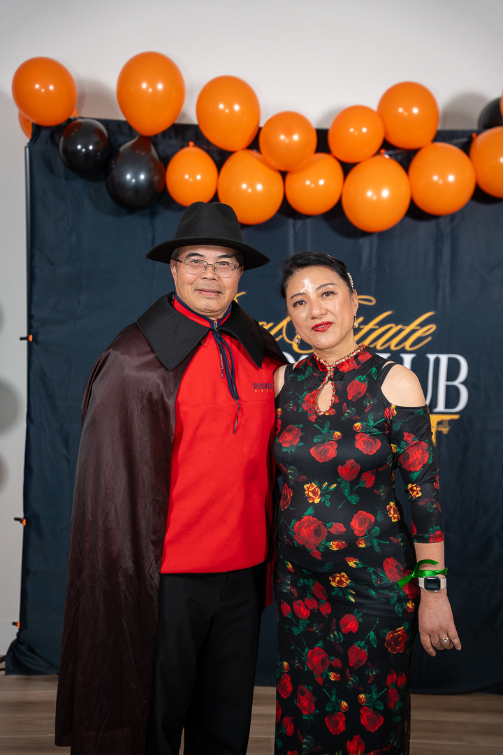 Guests in vampire and floral costumes posing beneath the orange and black balloons