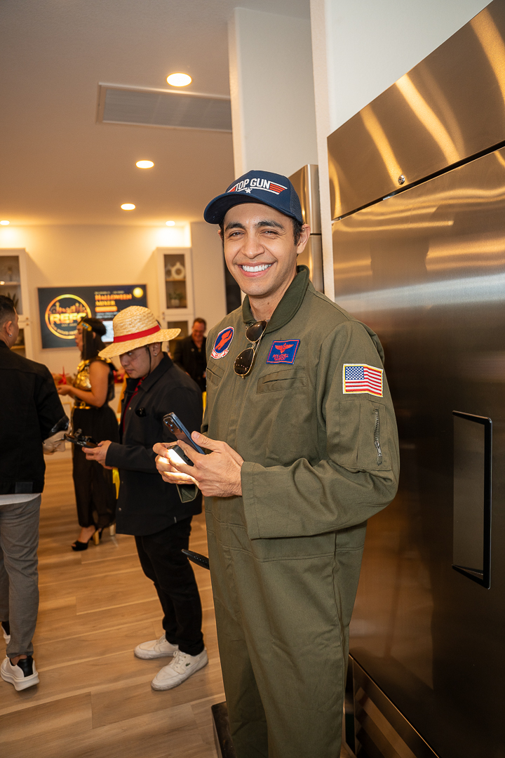 A guest in a flight-suit costume and aviator cap smiling beside the kitchen