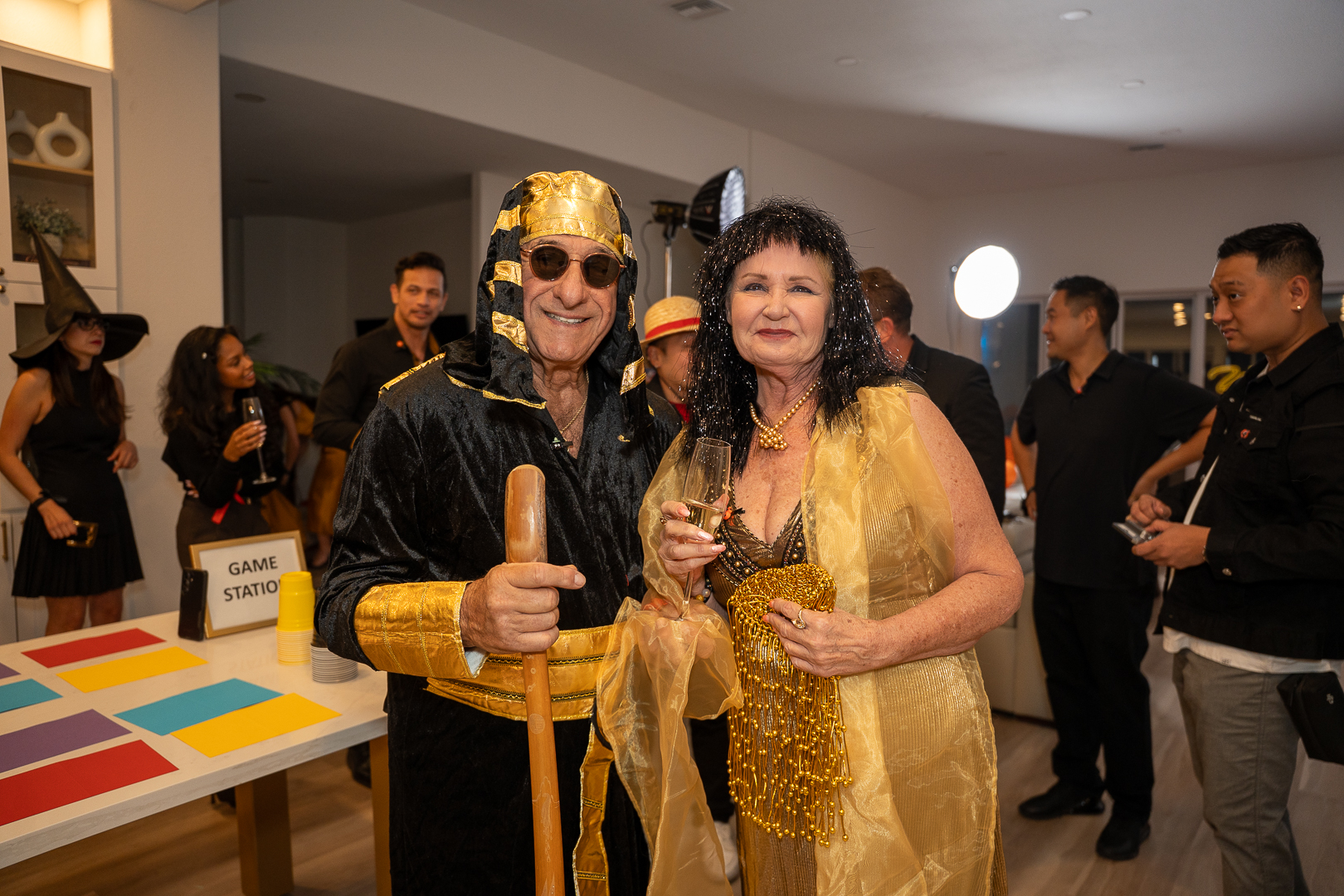 Two guests in gold costumes posing with drinks, one holding an Egyptian-style staff