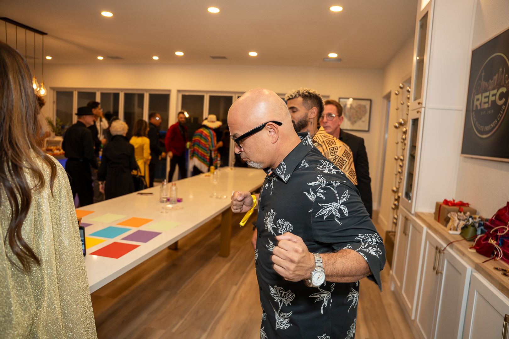 The mixer crowd filling the kitchen while a guest in a patterned shirt steps past