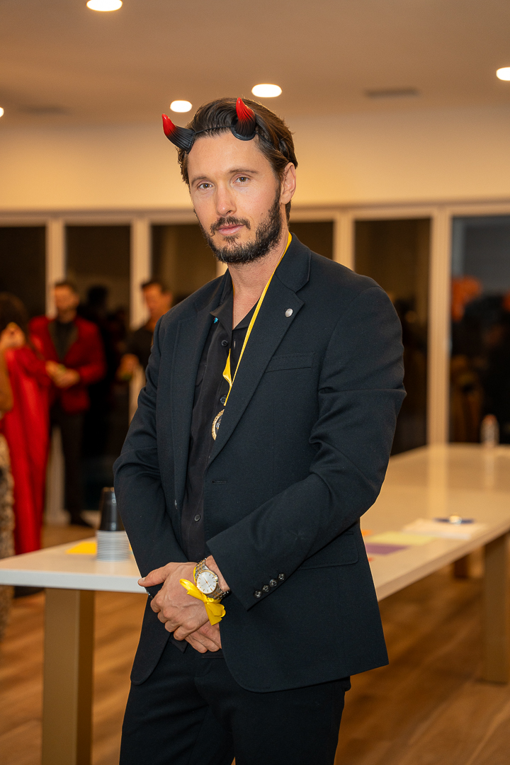 A guest in a black suit and red devil horns posing at the mixer