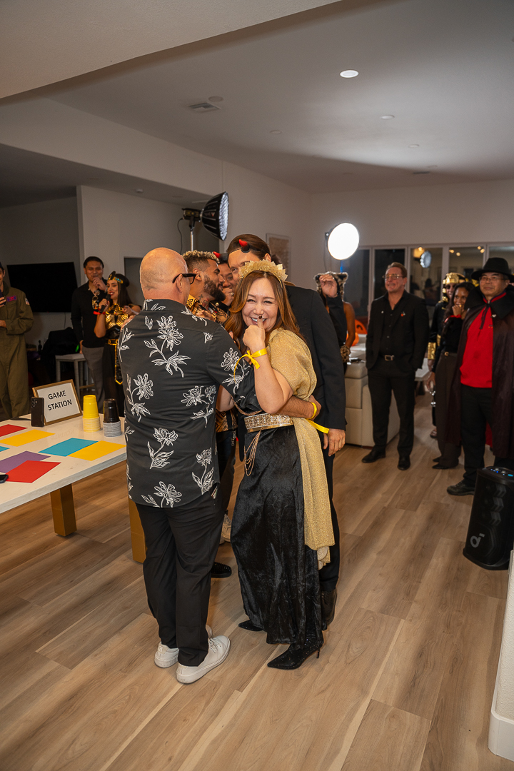 Friends sharing a hug as costumed guests mingle at the REFC anniversary party