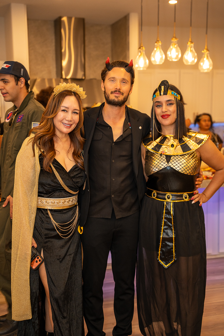 Three friends in black-and-gold Halloween outfits posing beside the kitchen island