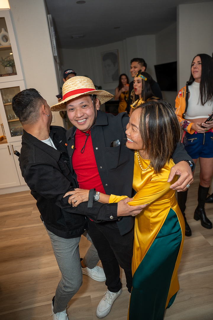 Guests sharing a laugh, including a guest in a straw hat and red scarf
