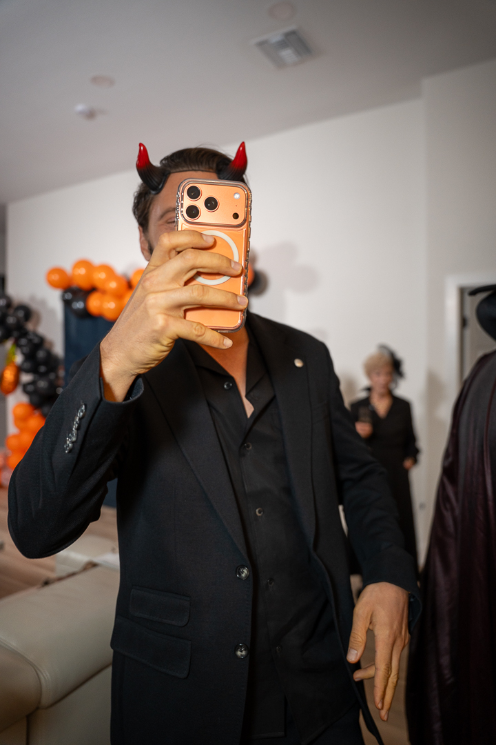 A guest in a dark suit and red devil horns capturing a moment on his phone