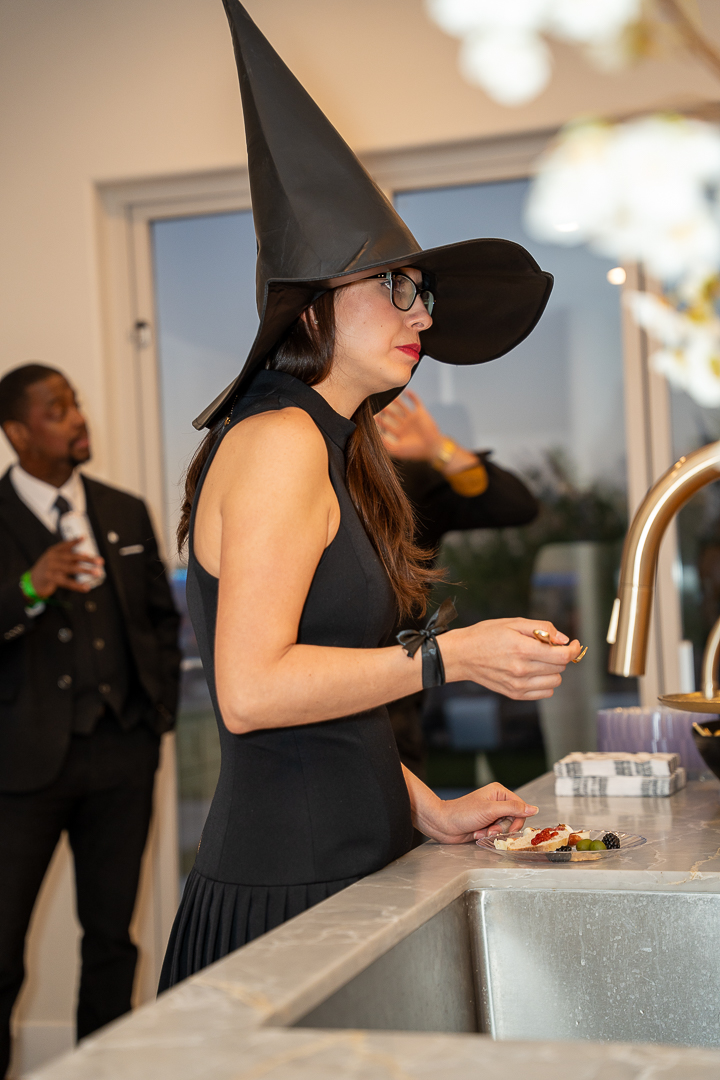 A guest in a witch costume enjoying refreshments beside the kitchen sink