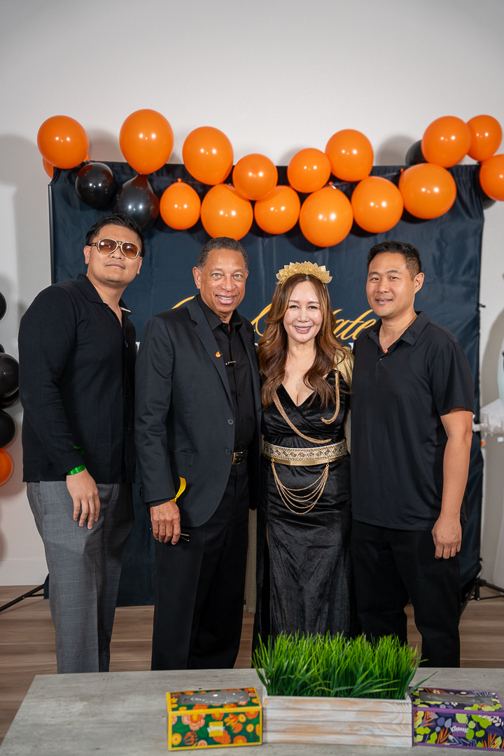 Four friends posing at the REFC backdrop beneath the orange and black balloons