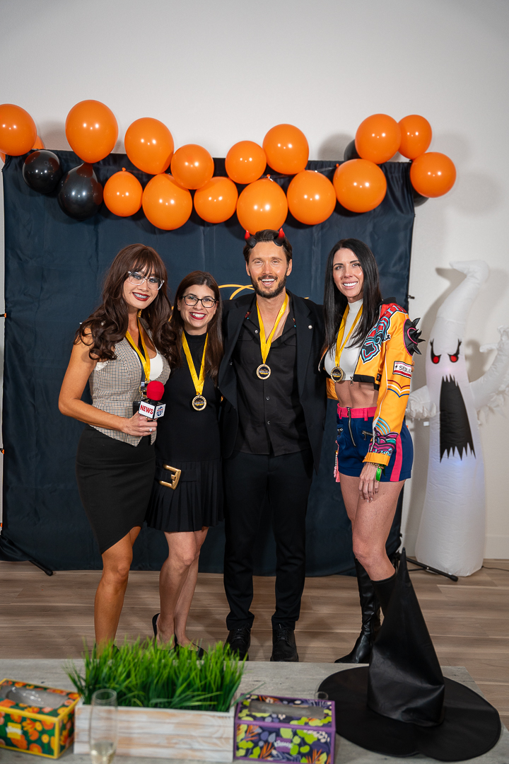 Five friends wearing medals posing beneath the orange and black balloons
