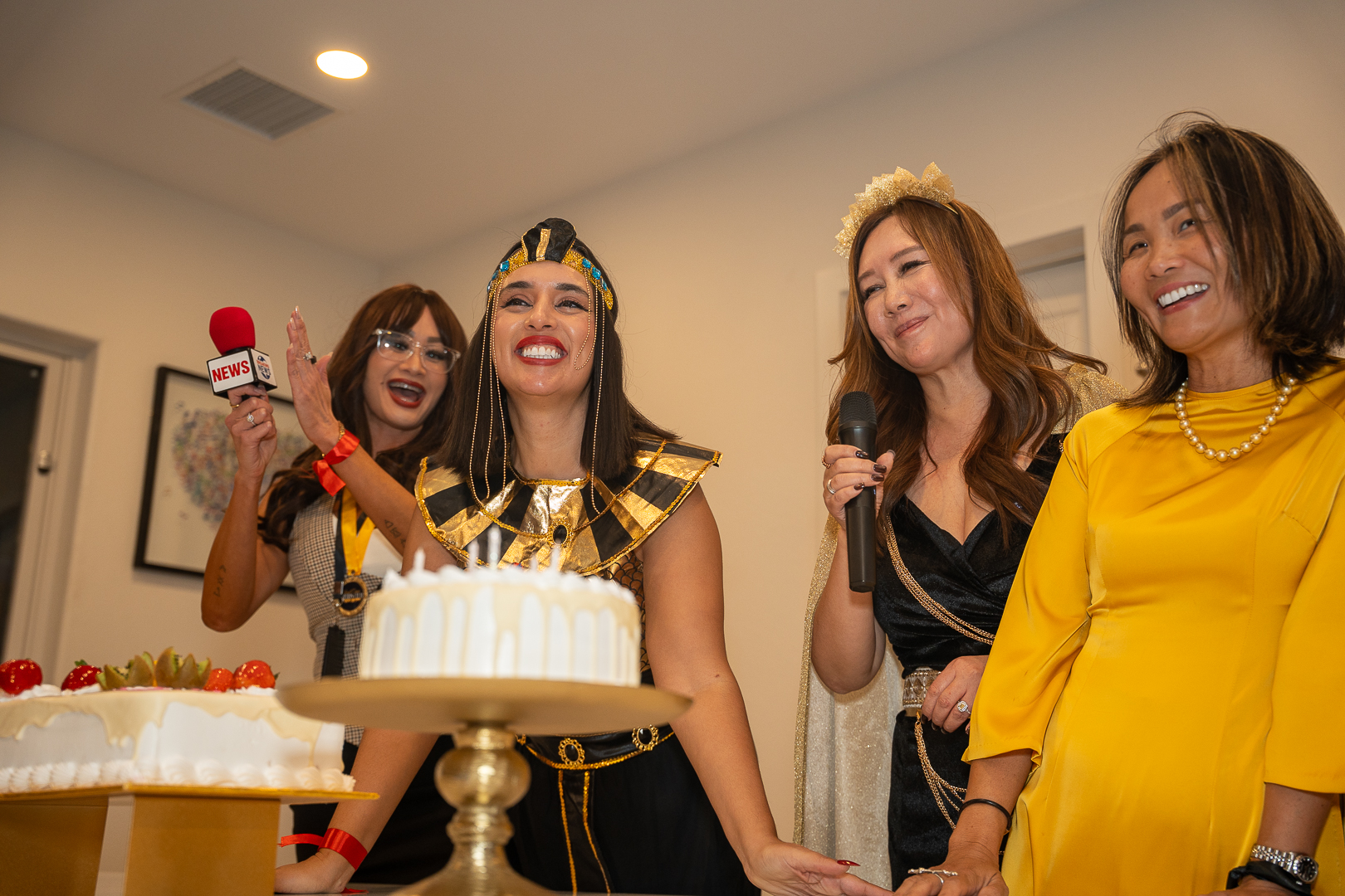 Costumed friends gathered beside the anniversary cake with a red microphone