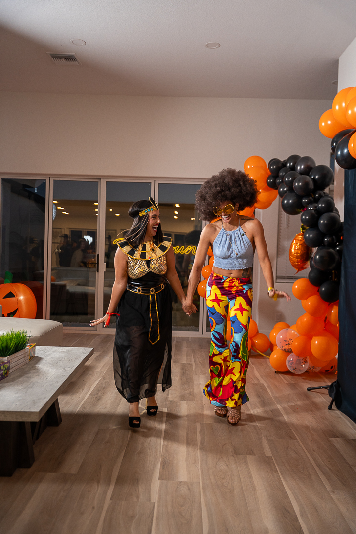 Two friends in Egyptian-inspired and colorful disco costumes walking together at the party