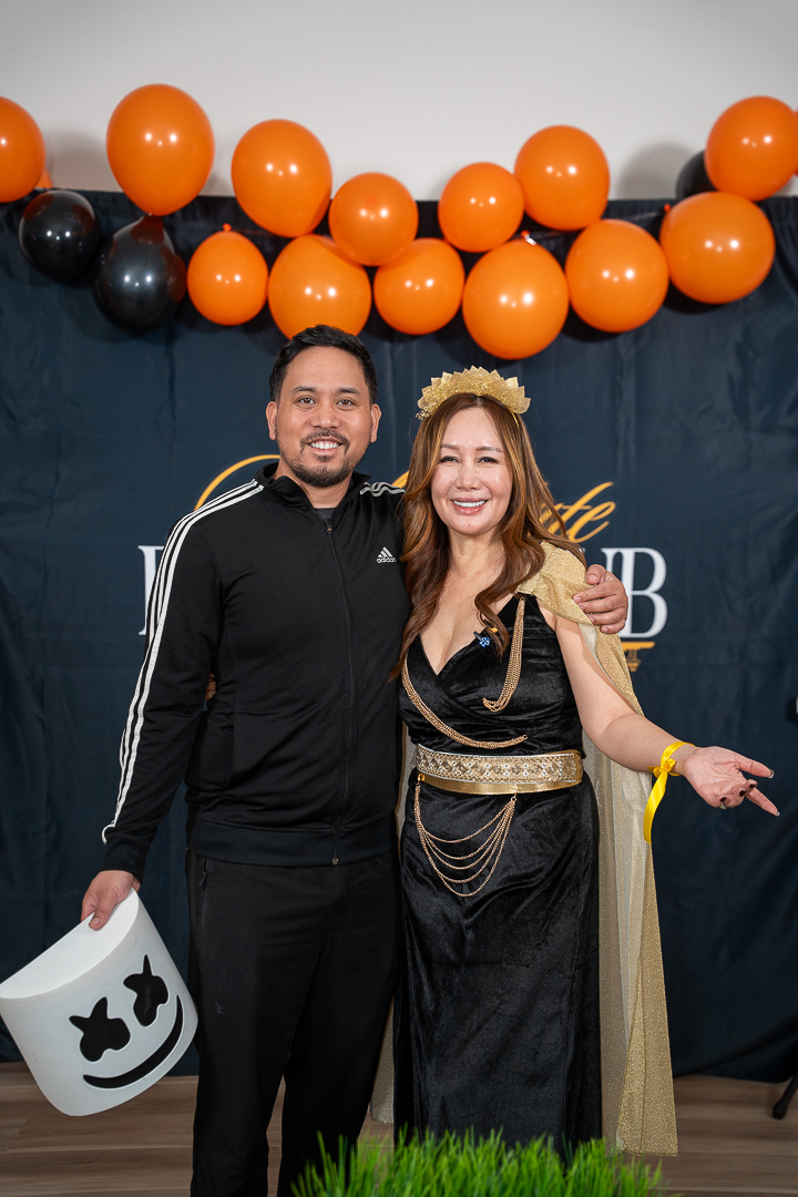 Two friends smiling together beneath the orange and black balloon arch