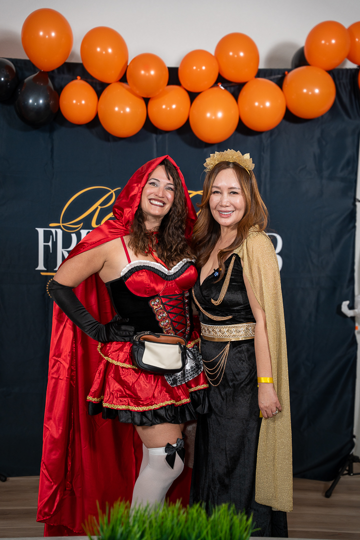 A guest as Little Red Riding Hood posing with the queen-costumed hostess at the backdrop