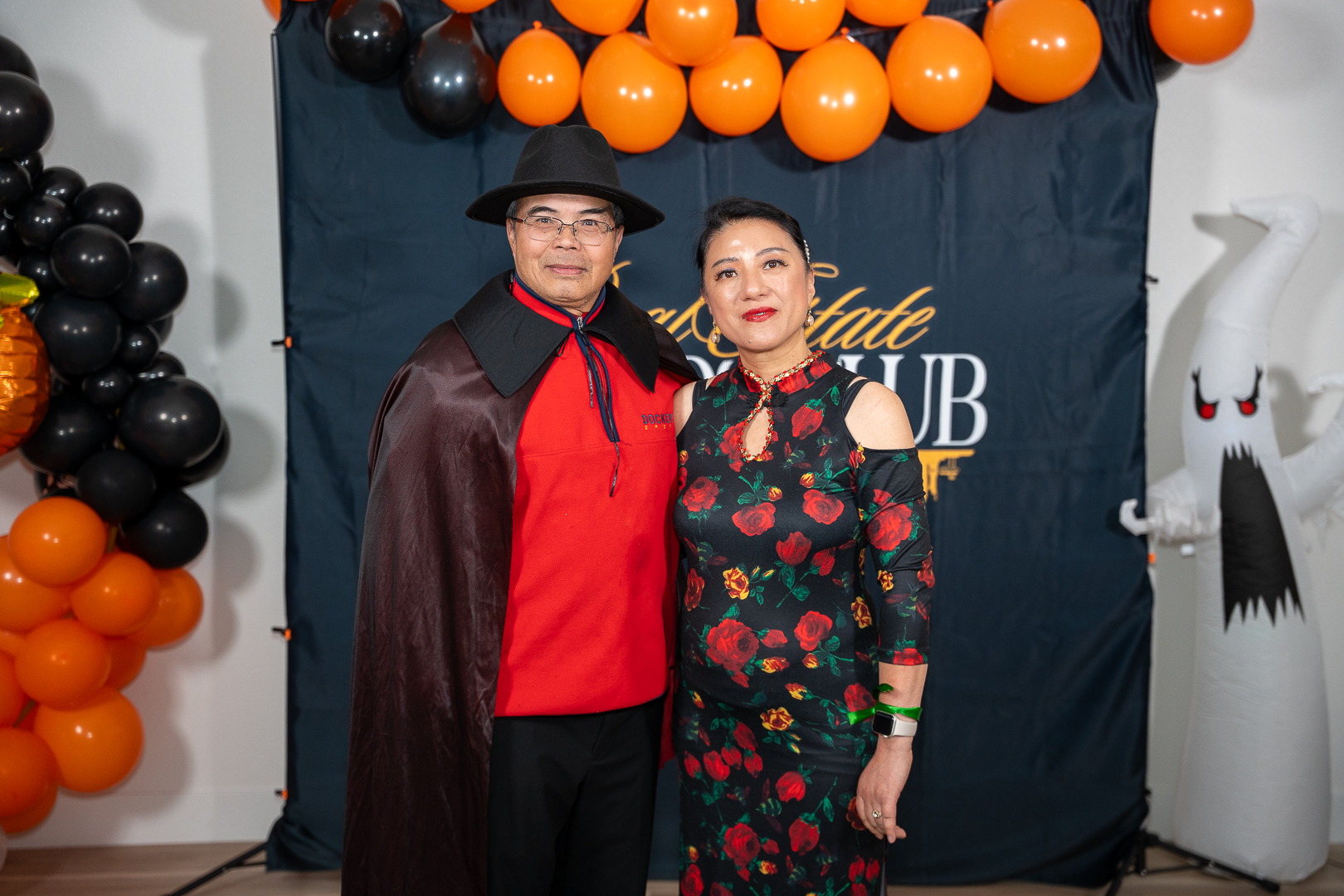 Two costumed friends posing at the REFC backdrop beneath the balloon arch