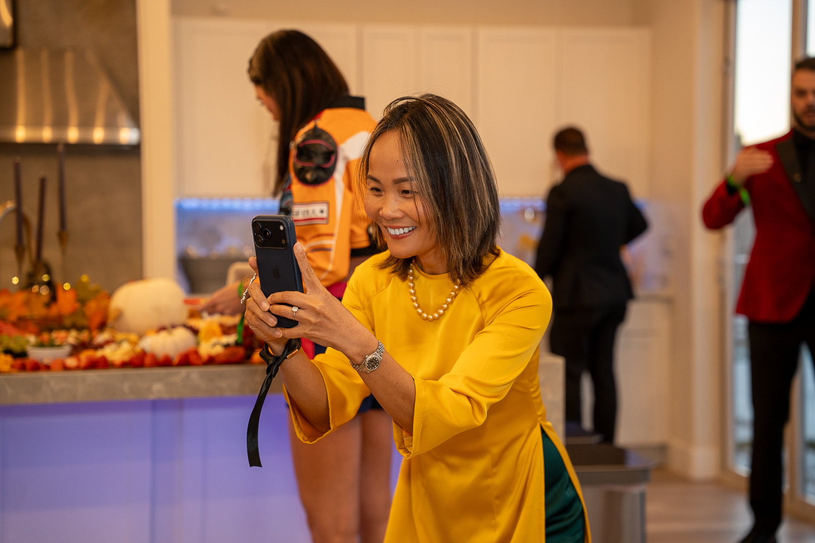A guest in a yellow áo dài taking a phone photo during the mixer