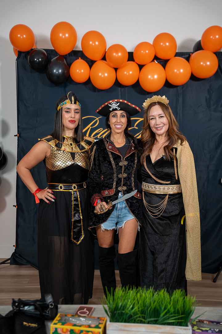 Three friends in Egyptian, pirate, and queen costumes posing at the REFC backdrop