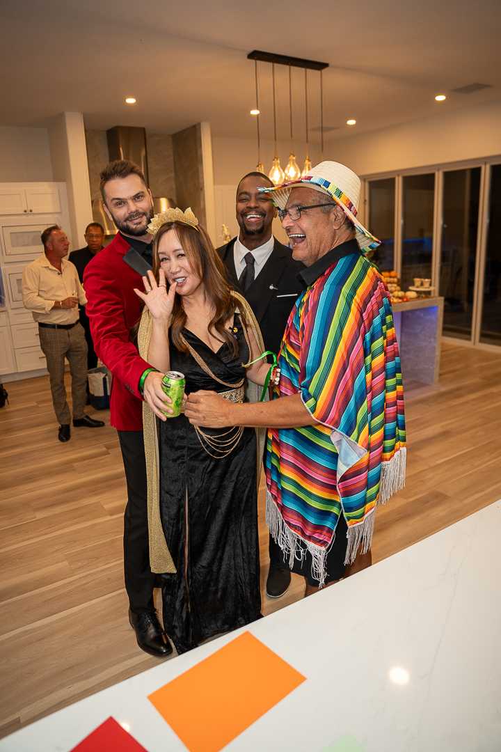 Smiling friends posing in Egyptian-inspired and colorful disco costumes beside the kitchen island