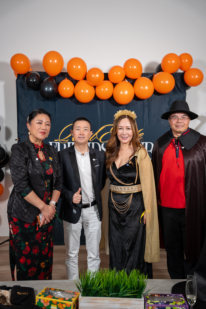 Four costumed friends posing beneath the orange and black balloon arch