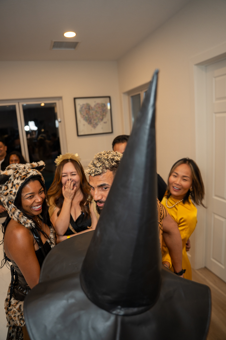 Friends laughing together beside a guest wearing a tall witch hat